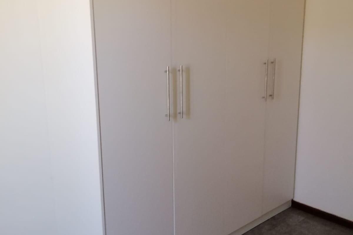 A clean, empty bedroom featuring neutral tiled flooring and a large, modern built-in wardrobe with sleek handles.