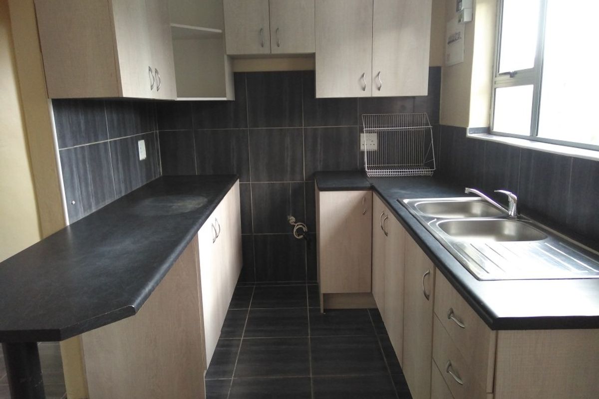 A functional kitchen featuring light-toned cabinetry, dark laminate countertops, a double stainless steel sink, and dark tiled splashbacks and flooring.