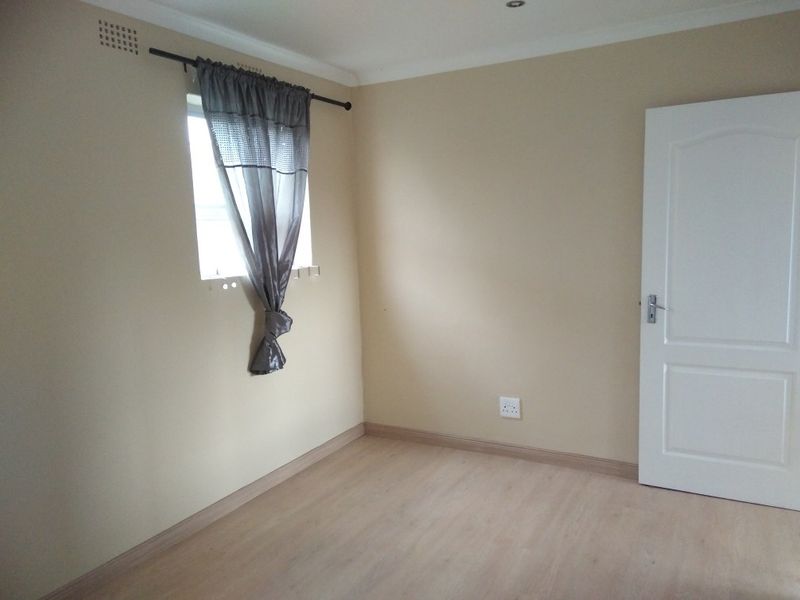 A clean, empty bedroom featuring light-toned laminate flooring, neutral wall paint, and a standard internal door.