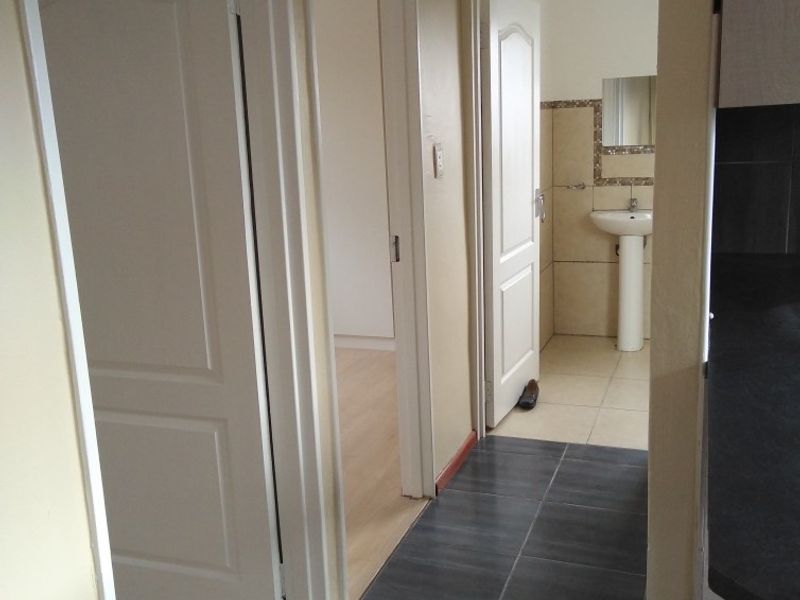 A functional hallway connecting multiple rooms, featuring a mix of tiled and laminate flooring with access to a bathroom with a pedestal sink.