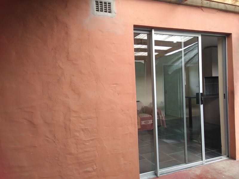 A covered patio area featuring a sliding glass door entrance, tiled flooring, and a timber pergola structure, with visible exterior wall plaster cracking.