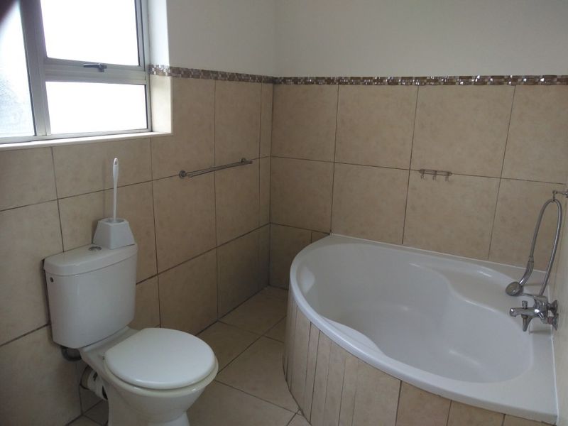 A functional bathroom featuring a built-in corner bathtub, a standard toilet, and neutral wall and floor tiling.