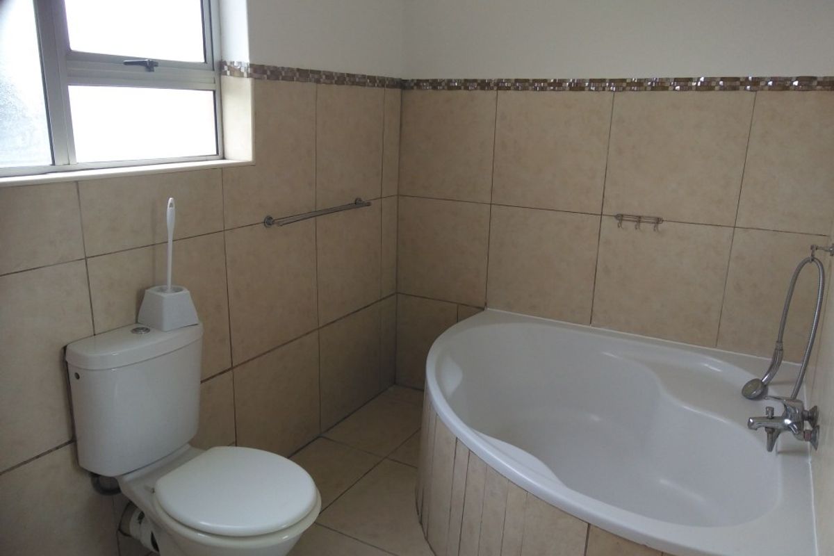 A functional bathroom featuring a built-in corner bathtub, a standard toilet, and neutral wall and floor tiling.