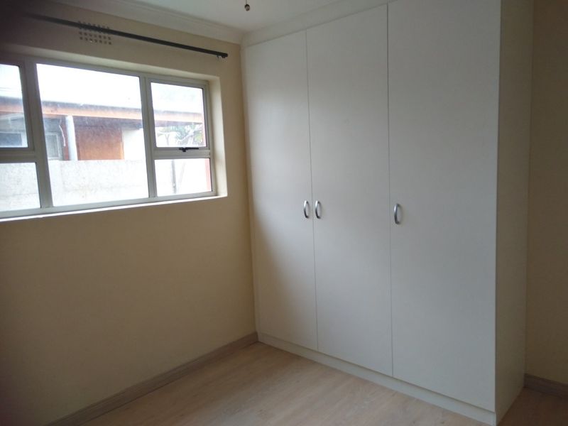 A clean, empty bedroom featuring neutral walls, laminate flooring, and ample built-in cupboard storage with a window providing natural light.
