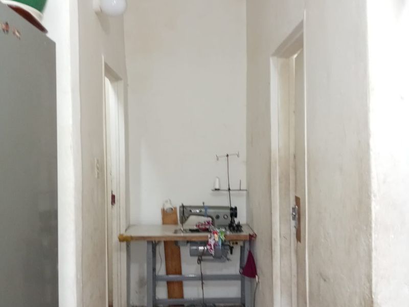 A narrow hallway featuring tiled flooring and wall-mounted lighting, showing signs of wear and requiring cosmetic updates to the wall finishes.