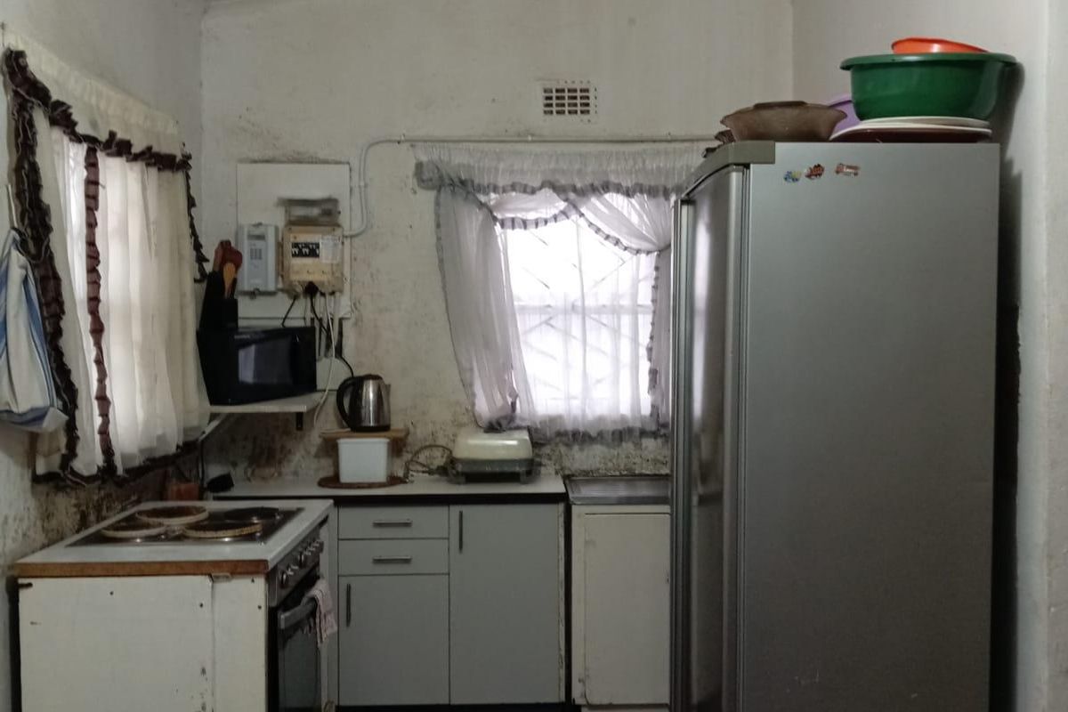 A compact kitchen featuring built-in cabinetry, an electric oven and hob, and tiled flooring, currently requiring cosmetic updates and refurbishment.