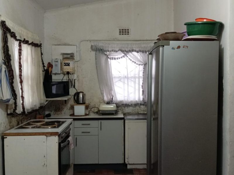 A compact kitchen featuring built-in cabinetry, an electric oven and hob, and tiled flooring, currently requiring cosmetic updates and refurbishment.