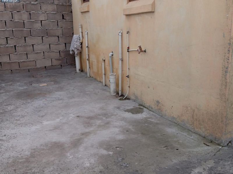 Rear exterior area featuring concrete paving, exposed plumbing infrastructure, and a cinder block boundary wall.