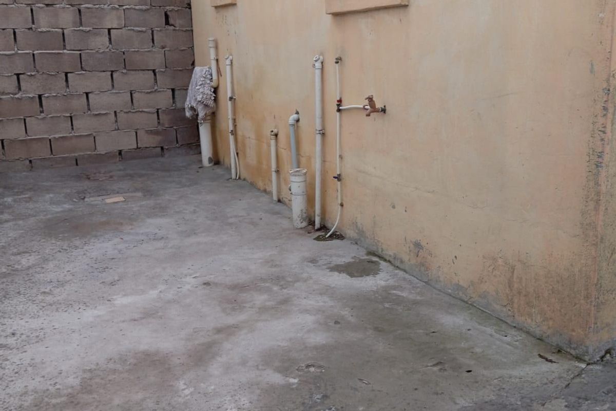 Rear exterior area featuring concrete paving, exposed plumbing infrastructure, and a cinder block boundary wall.
