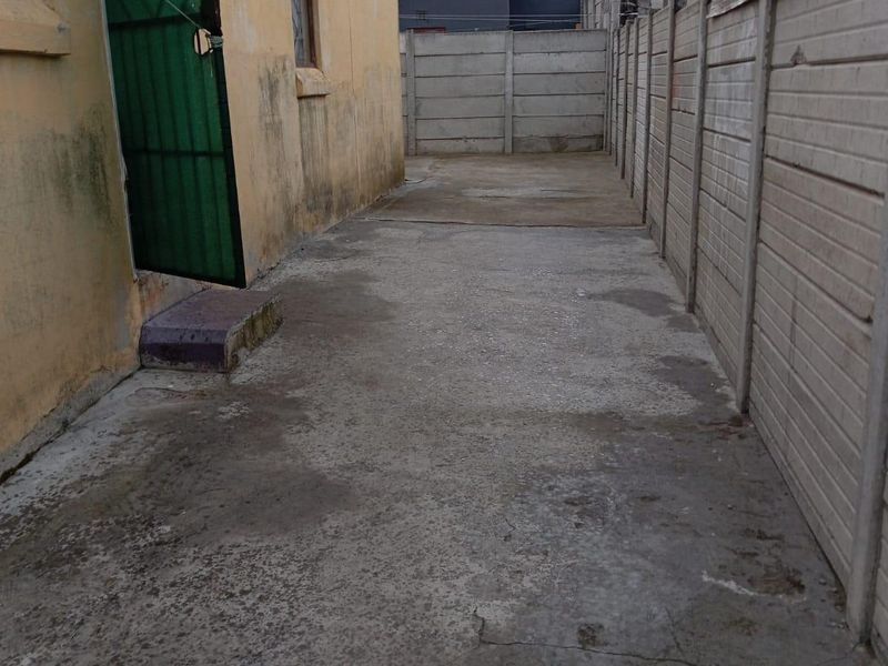 A narrow rear exterior area featuring concrete paving and a precast concrete boundary wall, showing signs of wear and weathering.