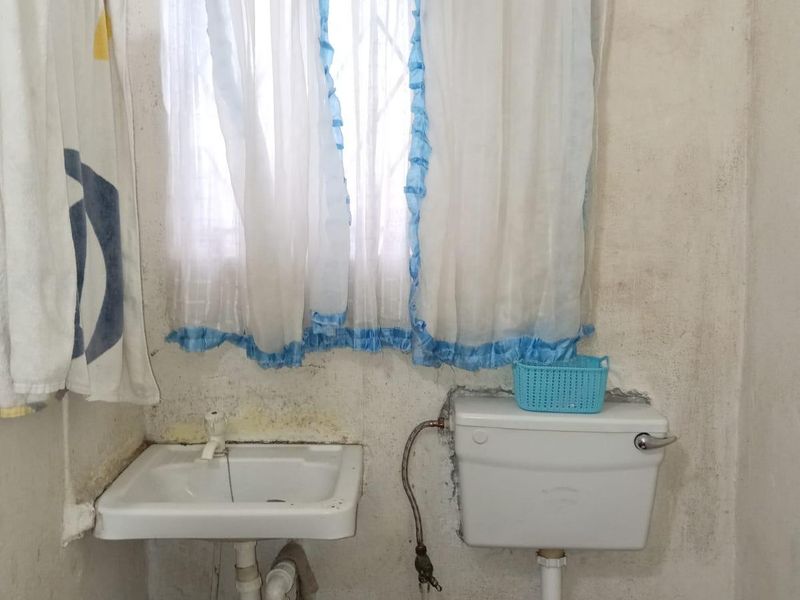 A small bathroom featuring a wall-mounted basin and flush toilet, requiring significant renovation and cosmetic updates to the wall finishes and fixtures.