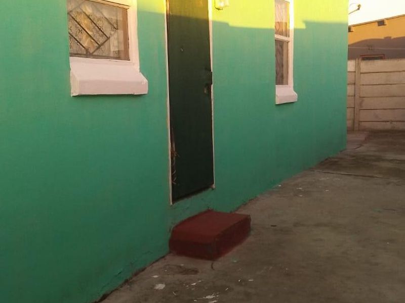 Rear exterior view of the property featuring a painted facade, security-barred windows, and a concrete paved area with a boundary wall.