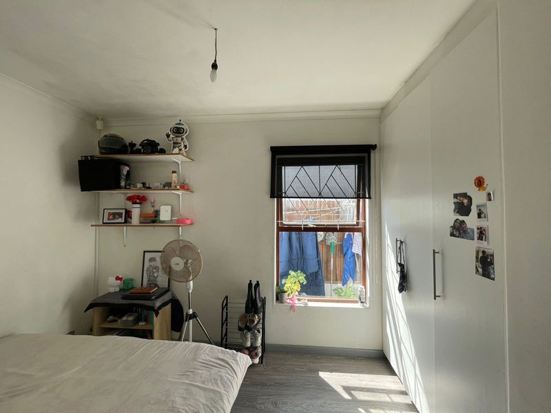 A bedroom featuring built-in wardrobes, laminate flooring, and a window with a roller blind, providing a functional and well-lit living space.