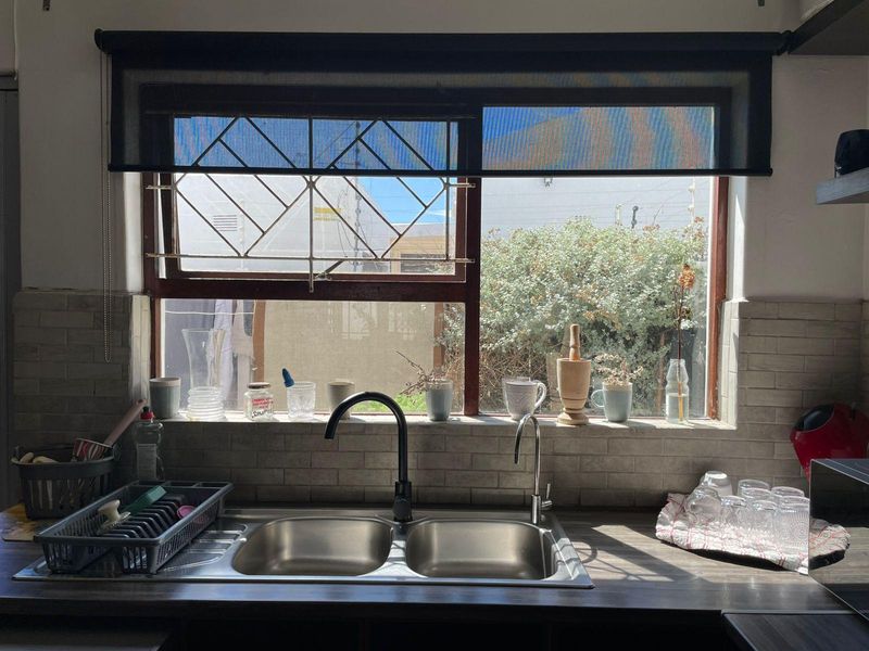 A functional kitchen sink area featuring a double bowl stainless steel sink, modern black mixer tap, and subway tile backsplash with natural light.