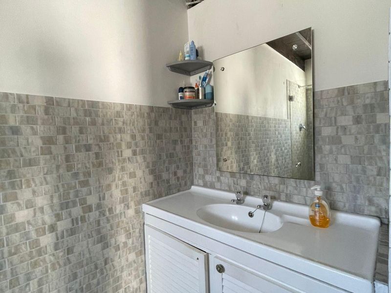A bathroom featuring a vanity cabinet with an integrated basin, tiled splashback, wall mirror, and exposed timber ceiling beams.