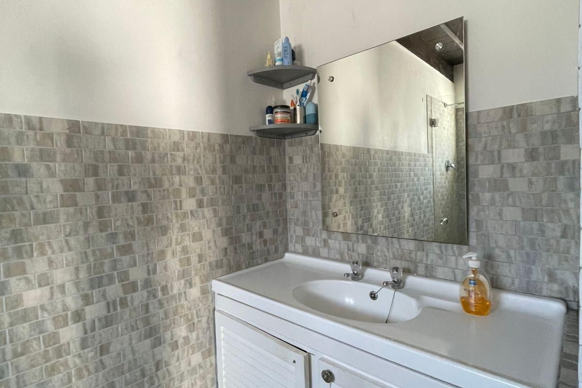 A bathroom featuring a vanity cabinet with an integrated basin, tiled splashback, wall mirror, and exposed timber ceiling beams.