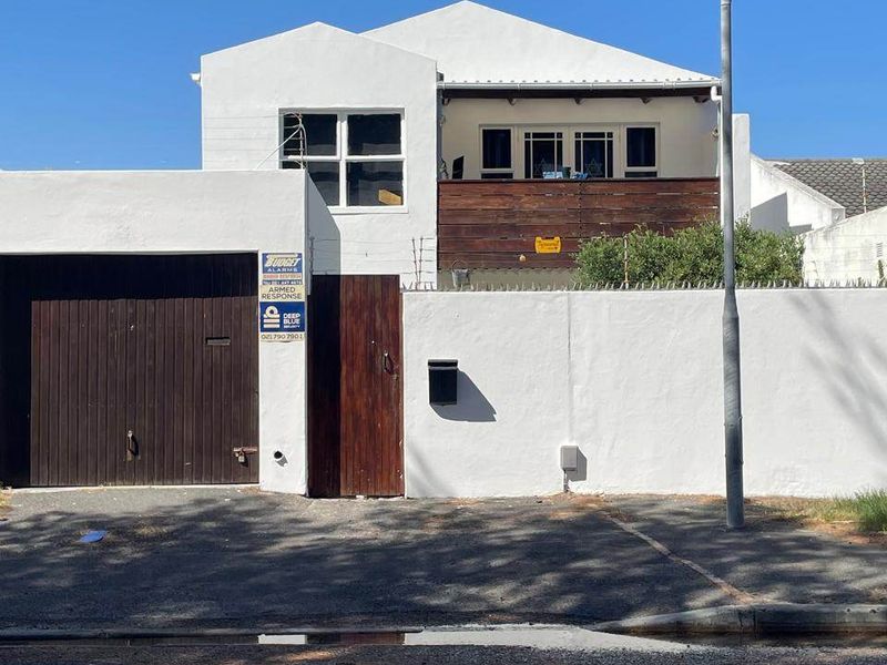 Front elevation of a two-story house featuring a garage, timber gate, boundary wall with security spikes, and an upper-level balcony with timber railing.