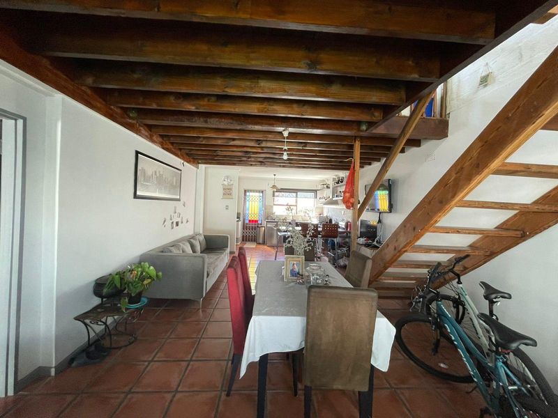 Open-plan living and dining area featuring exposed timber ceiling beams, a wooden staircase, and terracotta floor tiles leading to a functional kitchen space.