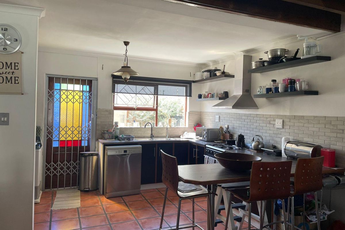 Functional kitchen featuring dark cabinetry, stainless steel appliances, tiled backsplash, and terracotta flooring, complemented by exposed ceiling beams and a secure entrance door.