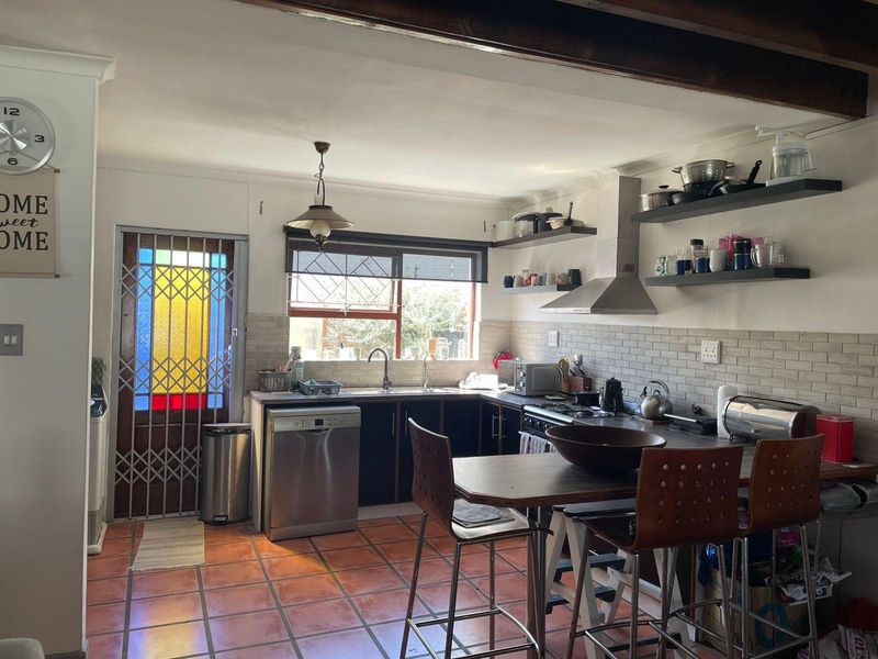 Functional kitchen featuring dark cabinetry, stainless steel appliances, tiled backsplash, and terracotta flooring, complemented by exposed ceiling beams and a secure entrance door.