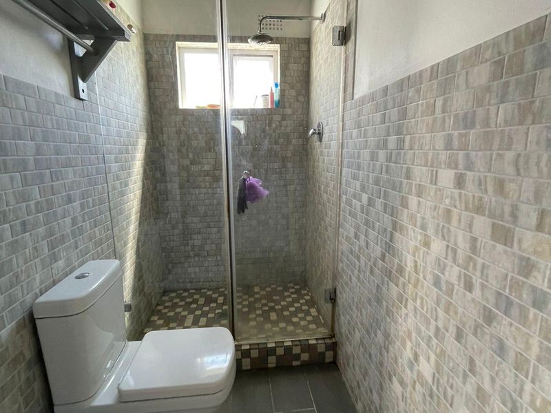 A functional bathroom featuring a walk-in shower with glass enclosure, tiled finishes, and exposed timber ceiling beams.