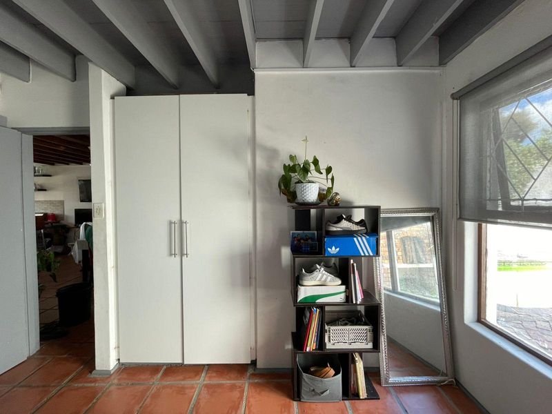 Bedroom featuring terracotta floor tiles, exposed beam ceiling, and a built-in cupboard with modern handles.