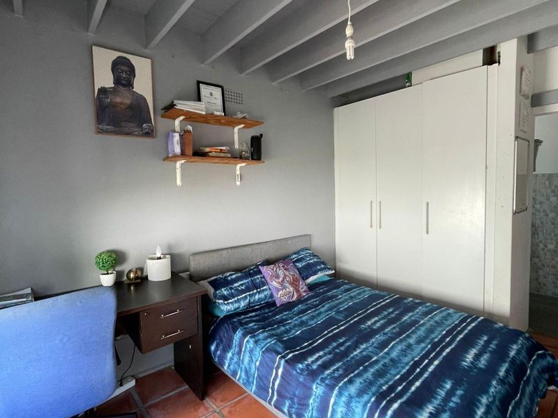 A bedroom featuring exposed ceiling beams, terracotta floor tiles, and a built-in wardrobe, offering a functional space with potential for aesthetic updates.