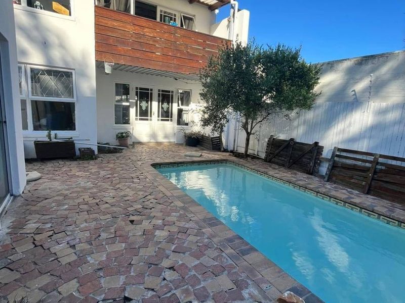 Rear exterior view featuring a swimming pool, paved patio area, and a two-story building facade with a wooden balcony.