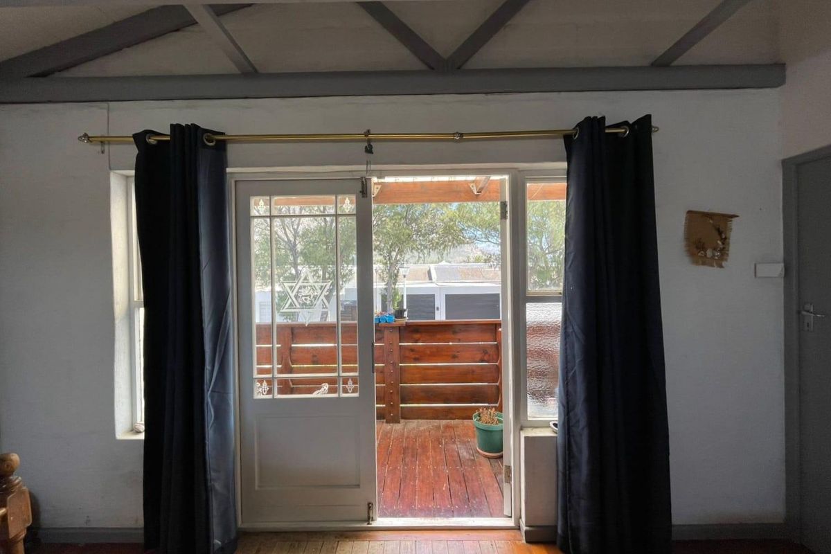 Living room featuring exposed timber ceiling beams and hardwood flooring, with direct access through a french door to an outdoor timber deck.