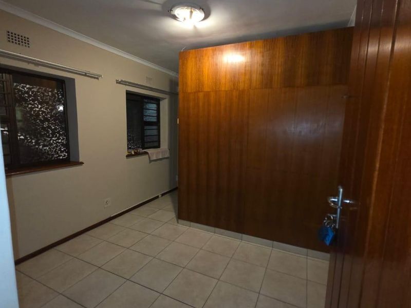 An empty bedroom featuring tiled flooring, built-in wooden cabinetry, and windows with security bars, offering a blank canvas for personalization.