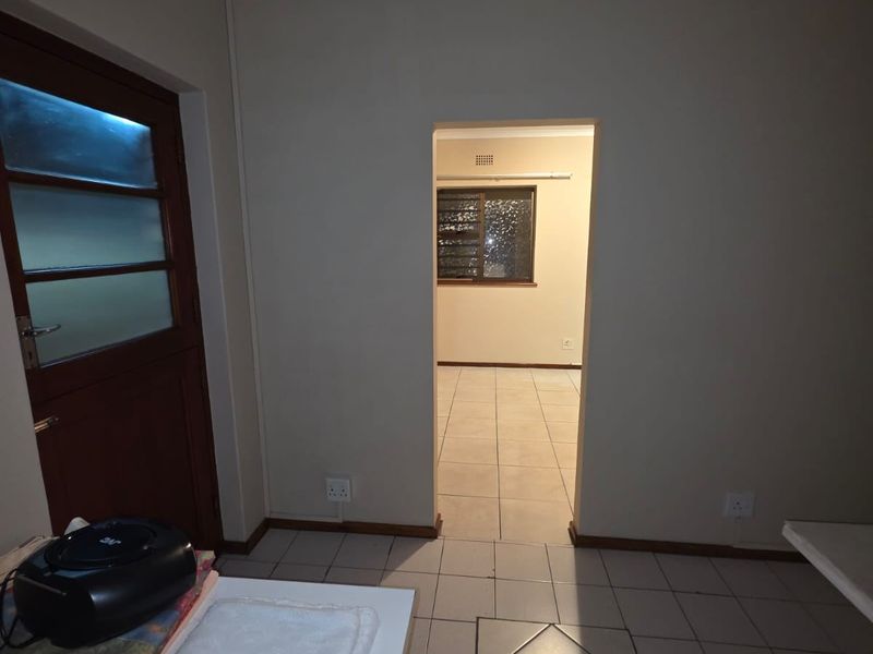 A neutral-toned hallway featuring tiled flooring and a doorway leading into an adjacent room with a louver window.