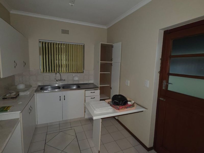 A functional kitchen featuring white built-in cabinetry, a double bowl stainless steel sink, tiled splashbacks, and ceramic floor tiles with direct exterior access.