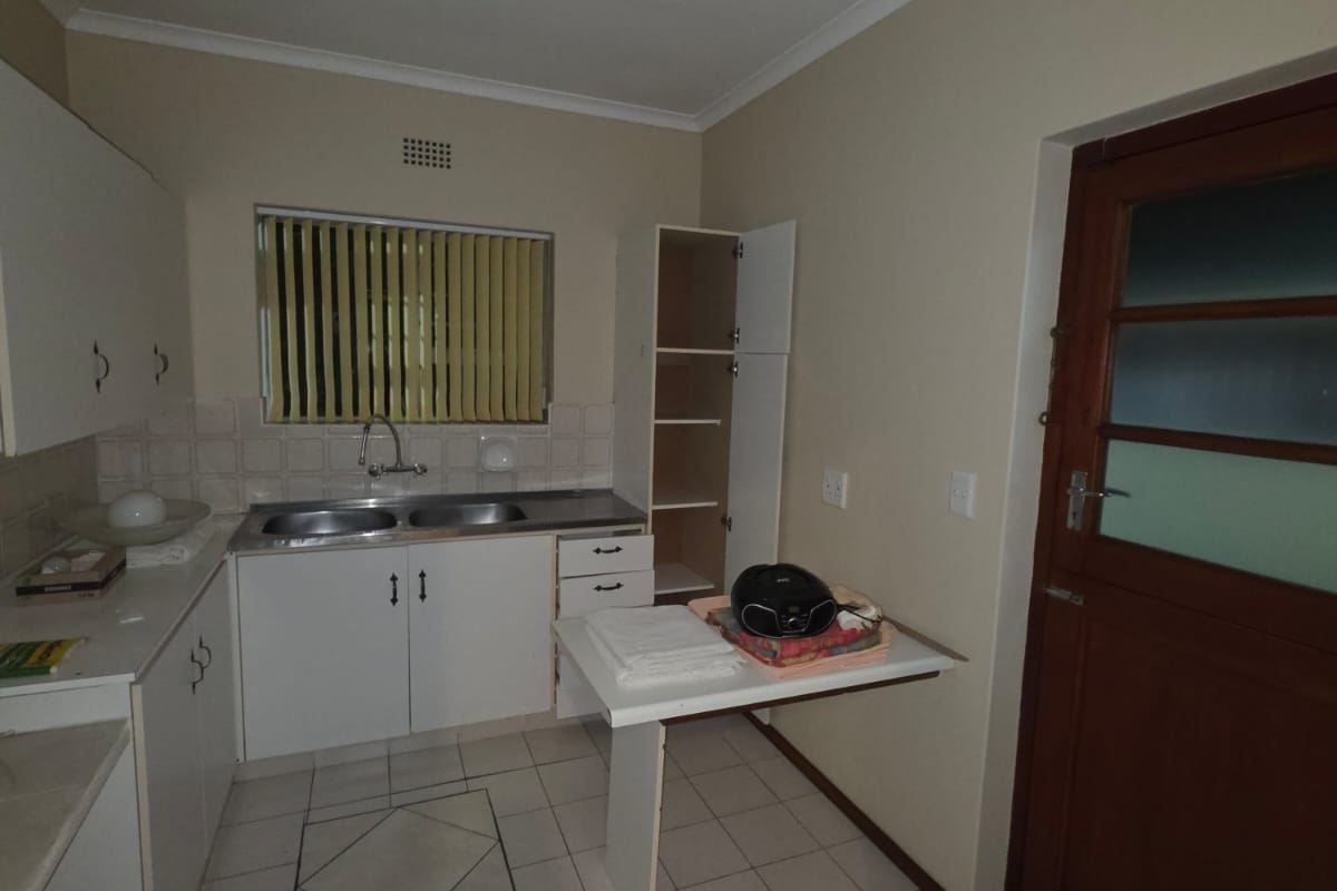 A functional kitchen featuring white built-in cabinetry, a double bowl stainless steel sink, tiled splashbacks, and ceramic floor tiles with direct exterior access.
