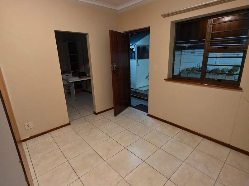 An empty living area featuring neutral tiled flooring, a timber door leading outside, and a window with an aluminium frame.