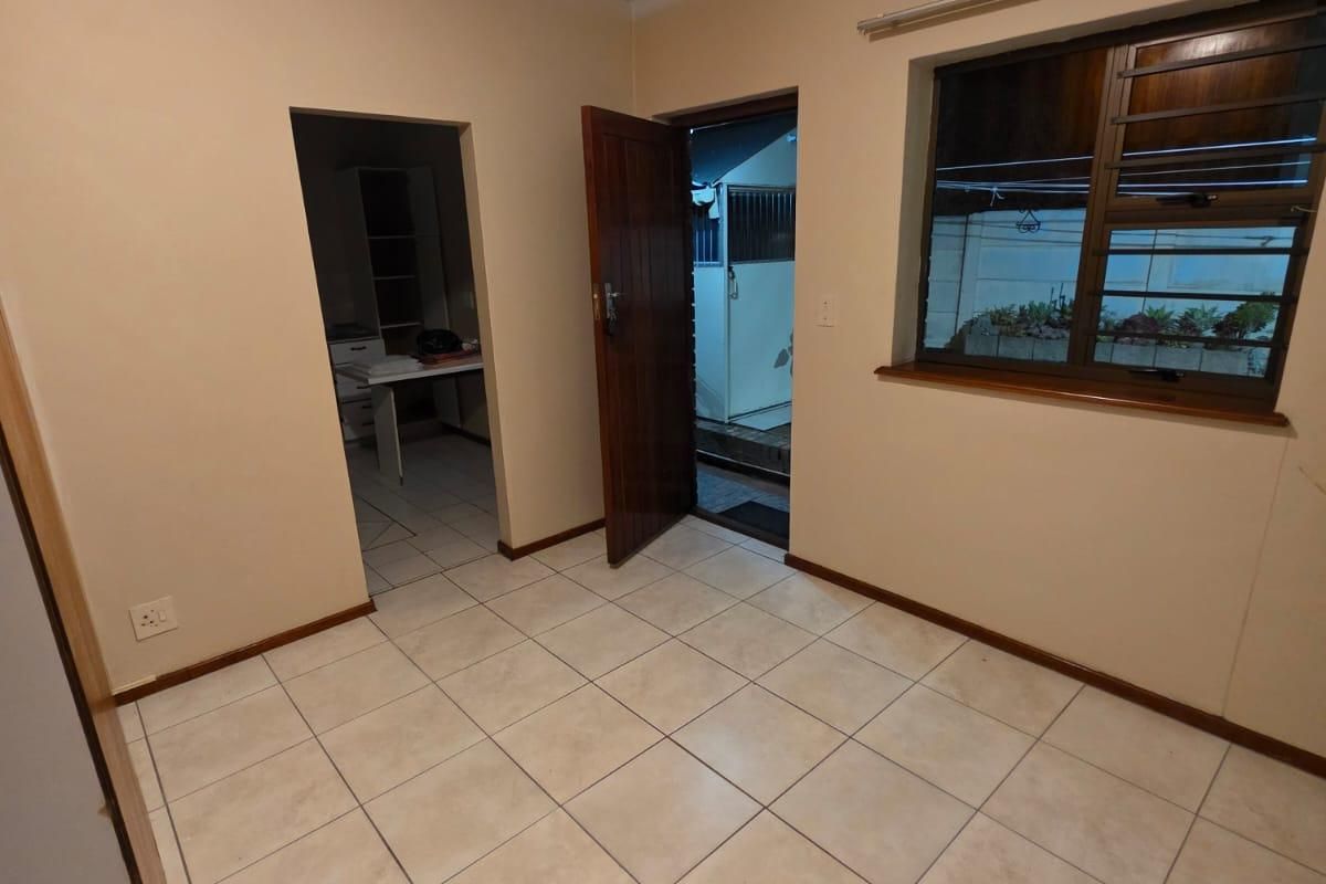 An empty living area featuring neutral tiled flooring, a timber door leading outside, and a window with an aluminium frame.