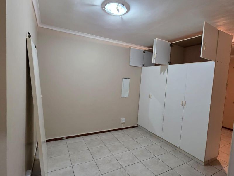 An empty bedroom featuring tiled flooring and built-in cupboards with some visible damage to the cabinetry doors.