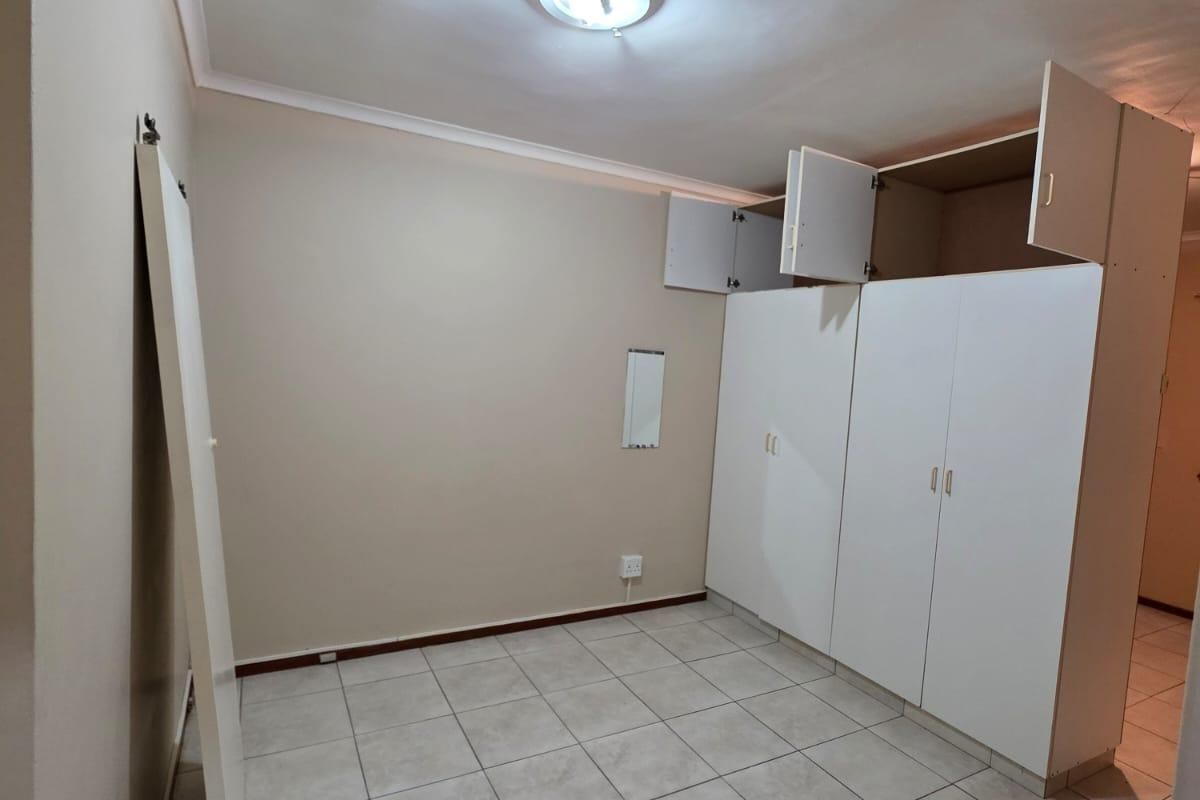 An empty bedroom featuring tiled flooring and built-in cupboards with some visible damage to the cabinetry doors.