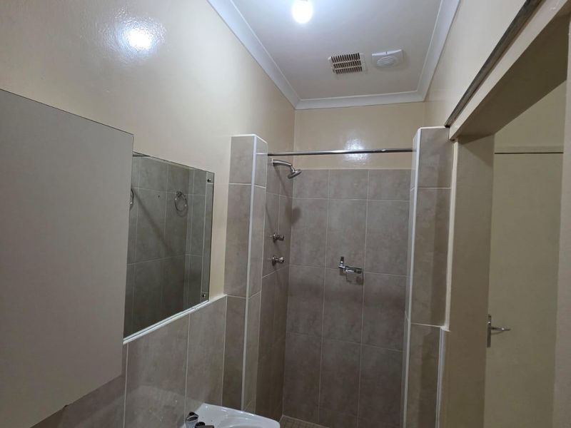A functional bathroom featuring a tiled walk-in shower, wall-mounted basin, and neutral wall finishes, presenting a clean and well-maintained space.