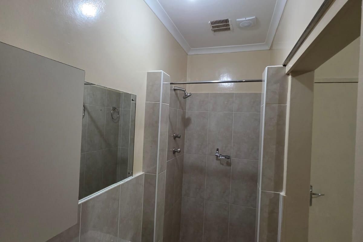 A functional bathroom featuring a tiled walk-in shower, wall-mounted basin, and neutral wall finishes, presenting a clean and well-maintained space.