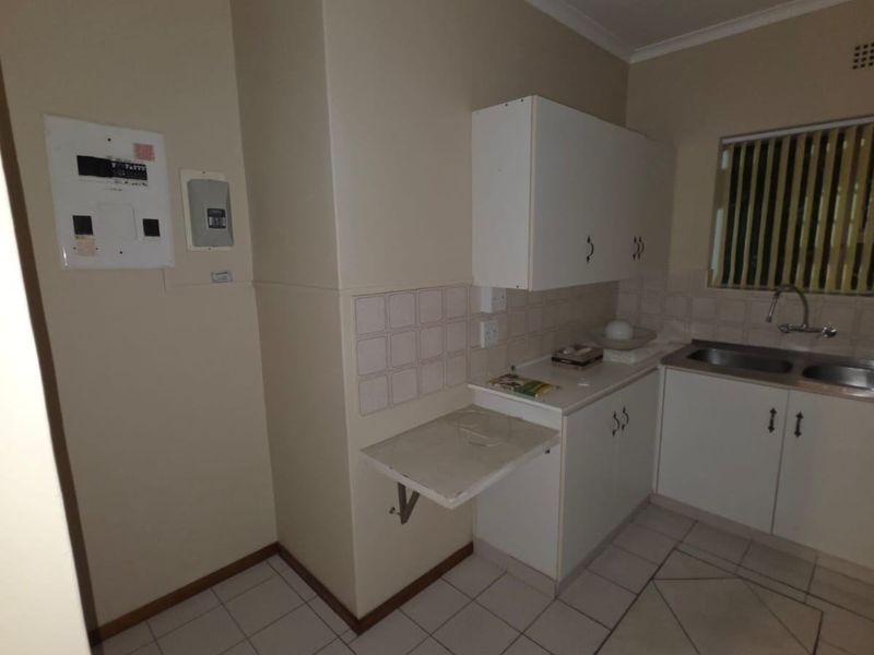 A compact kitchen featuring white built-in cabinetry, a double basin sink, tiled splashbacks, and a convenient fold-down wall table.