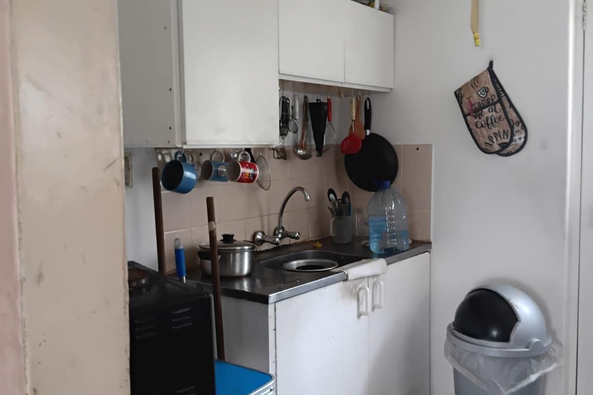 A compact kitchen area featuring basic wall and base cabinetry, a stainless steel sink, and tiled splashback, requiring cosmetic updates to improve functionality and aesthetics.