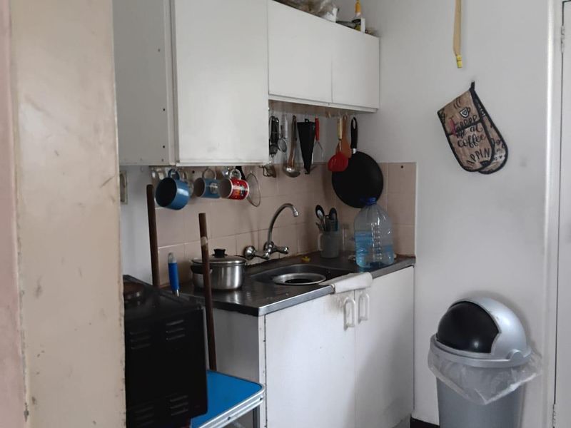 A compact kitchen area featuring basic wall and base cabinetry, a stainless steel sink, and tiled splashback, requiring cosmetic updates to improve functionality and aesthetics.