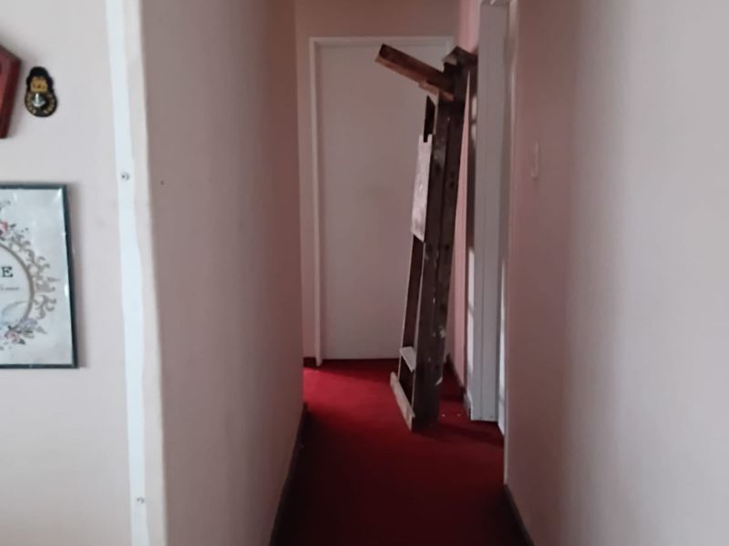 A narrow residential hallway featuring red carpeting and a ceiling access hatch, requiring cosmetic updates to improve the overall aesthetic.