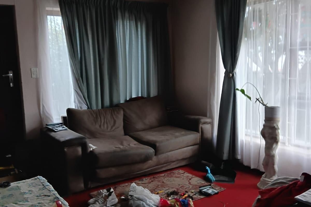 A living room featuring a ceiling fan and large windows with curtain rails. The space requires cosmetic updates to improve its overall condition.