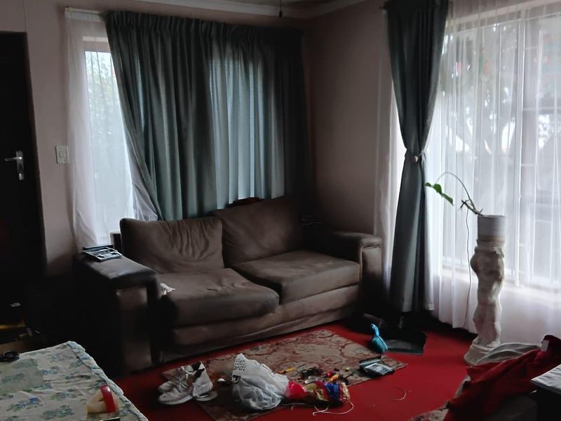 A living room featuring a ceiling fan and large windows with curtain rails. The space requires cosmetic updates to improve its overall condition.