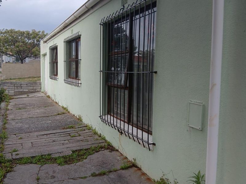 A side exterior view of the house featuring security bars on windows, guttering, and a concrete walkway showing signs of wear and weathering.