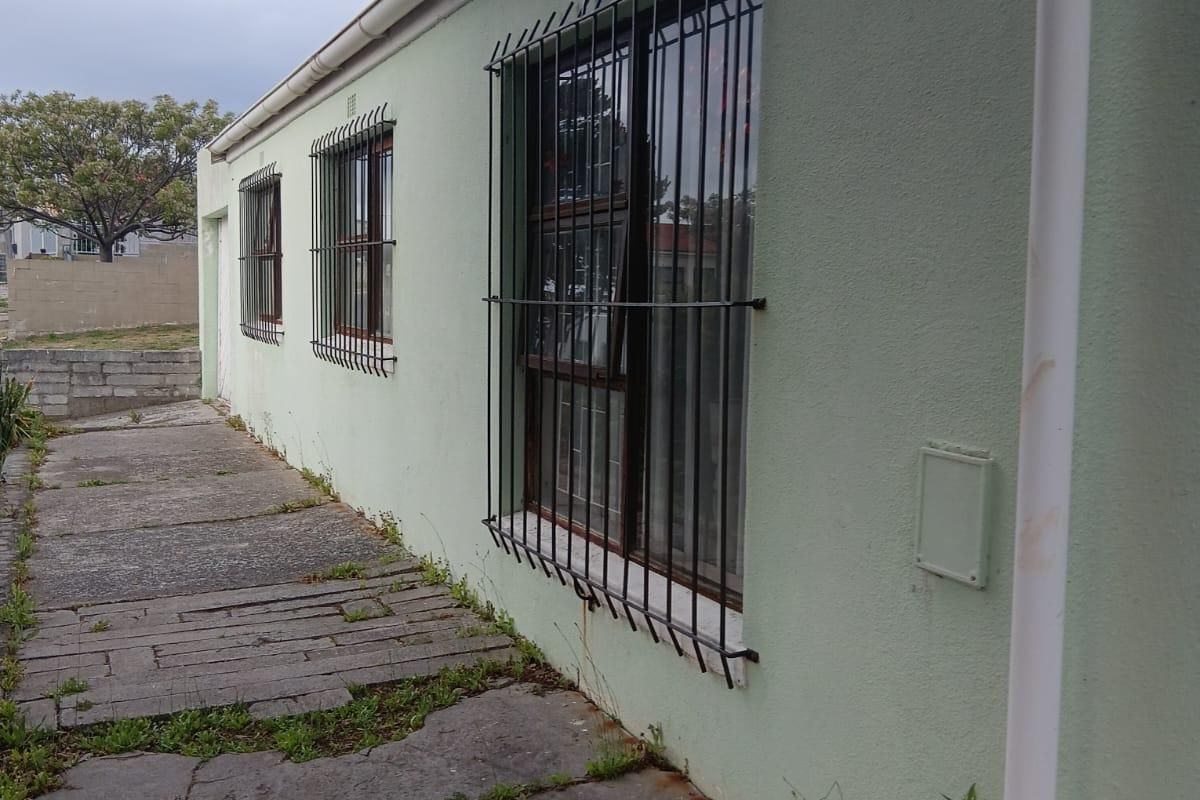 A side exterior view of the house featuring security bars on windows, guttering, and a concrete walkway showing signs of wear and weathering.