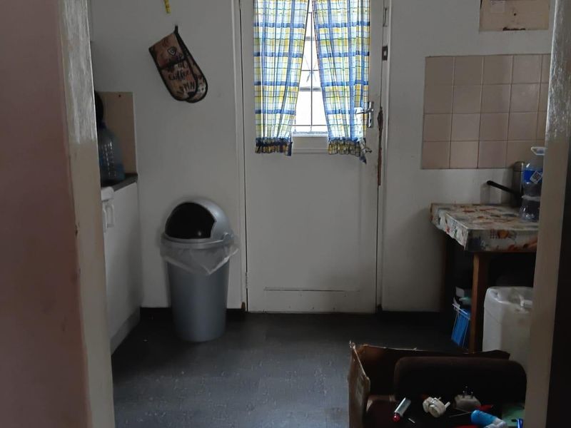 A functional kitchen area featuring a tiled splashback and direct exterior access, currently requiring cosmetic updates and improved finishes.