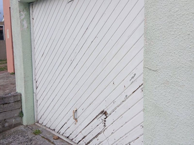 Exterior view of a garage featuring a weathered, damaged garage door and cracked concrete driveway, showing significant signs of wear and maintenance requirements.