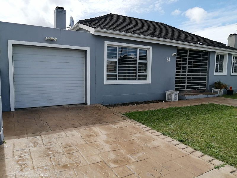 Front exterior view of a single-story house featuring a paved driveway, garage, and security bars on windows.